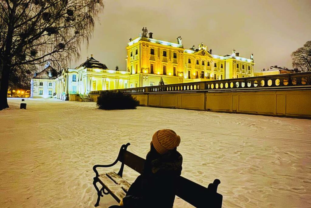 Kobieta odwiedzająca Białystok w ramach Podlaski Reset podziwia piękno Paacu Branickich zimową, wieczorowa porą, delektując się spokojem w rytmie slow.