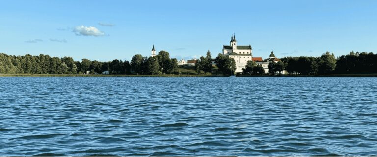 Widok z pokładu łodzi na Klasztor Pokamedulski wyłaniający się w dali nad jeziorem Wigry – Wigierski Park Narodowy, podczas mikrowyprawy Pojezierze Suwalsko-Augustowskie z samimunay