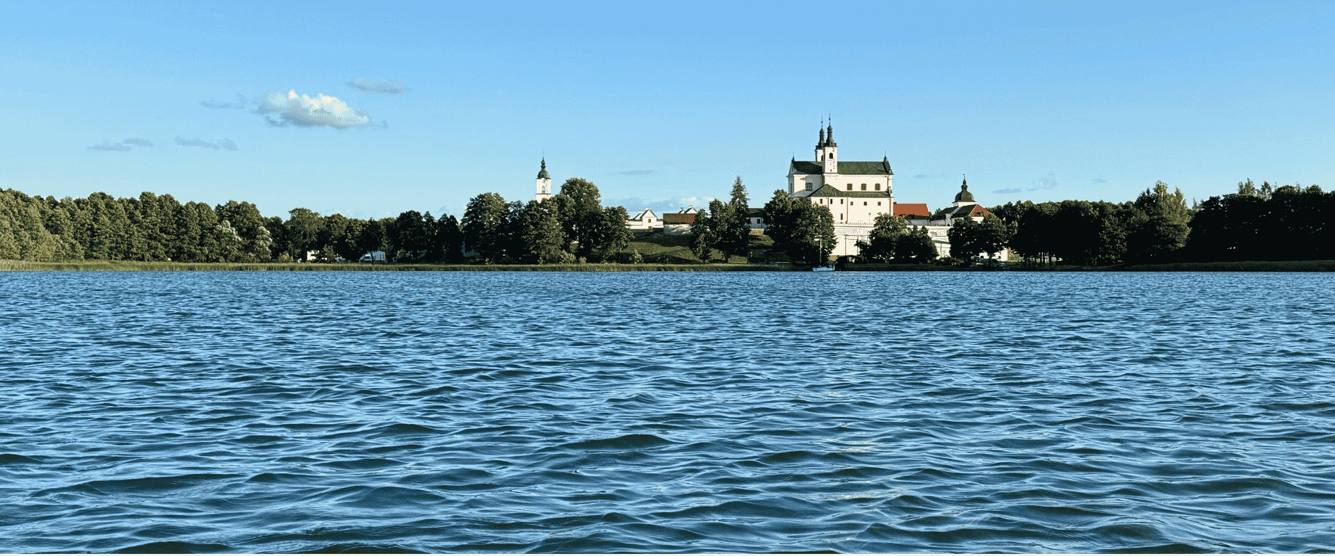 Widok z pokładu łodzi na Klasztor Pokamedulski wyłaniający się w dali nad jeziorem Wigry – Wigierski Park Narodowy, podczas mikrowyprawy Pojezierze Suwalsko-Augustowskie z samimunay